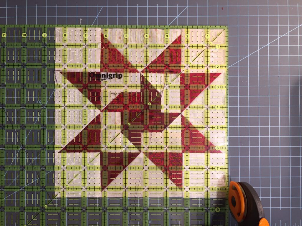 trimming quilt block with rotary cutter and plastic ruler on cutting mat