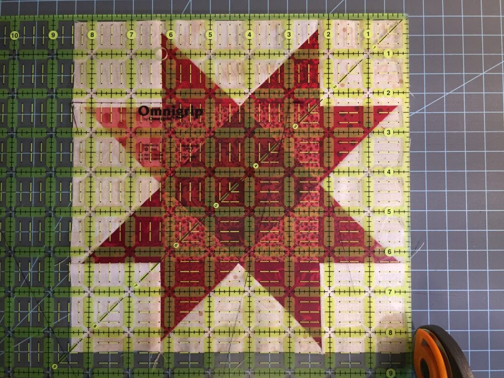 trimming square in a square sawtooth star quilt block with rotary cutter and plastic ruler
